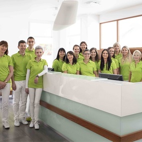 Das Praxisteam einer modernen Zahnarztpraxis steht lächelnd an der Rezeption.